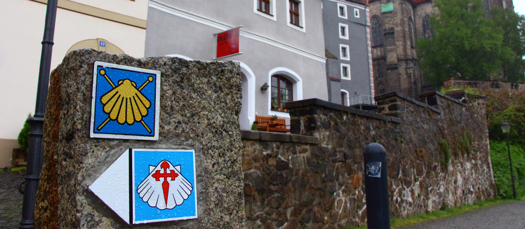 Eine Straße, die an der Kirche in Görlitz vorbei führt. Im Fordergrund die Wegmarkierungen der Pilgerstrecke.
