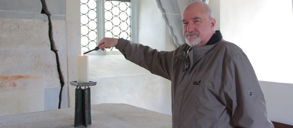 Ein brätiger Mann steh in einer hellen Kapelle und zündet eine Kerze an.