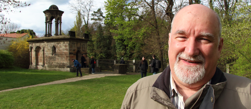 Ein bärtige Mann steht vor einer Kopie des Grabes Christi.