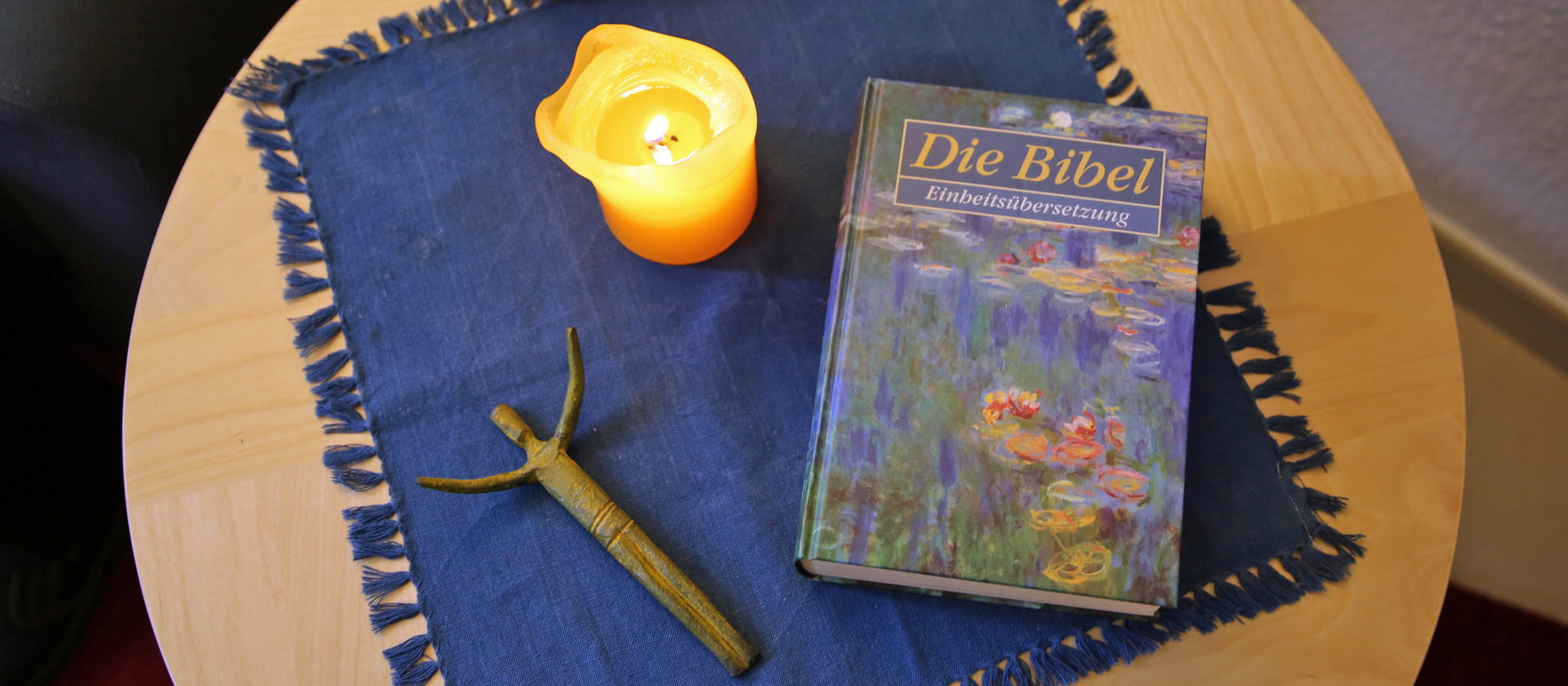 Eine Bibel, eine Kerze und ein Kreuz liegen auf dem Tisch.