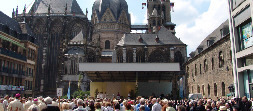 Vor dem Aachener Dom ist ein großer Altar aufgebaut. Davor ist eine Menschenmenge versammelt.