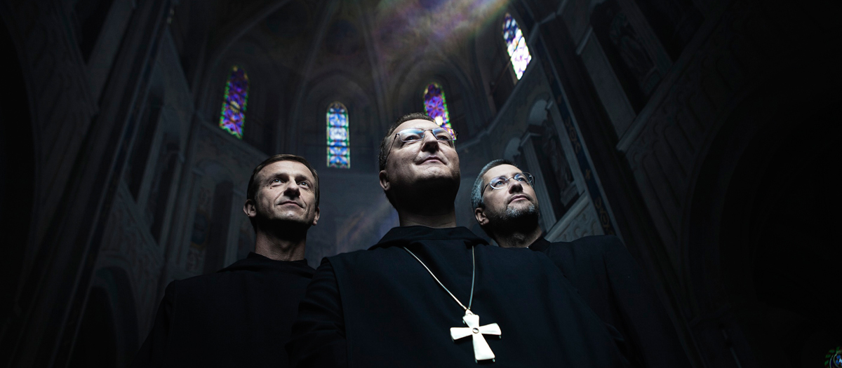 Drei Priester in schwarzen Roben in einer dunklen Kirche