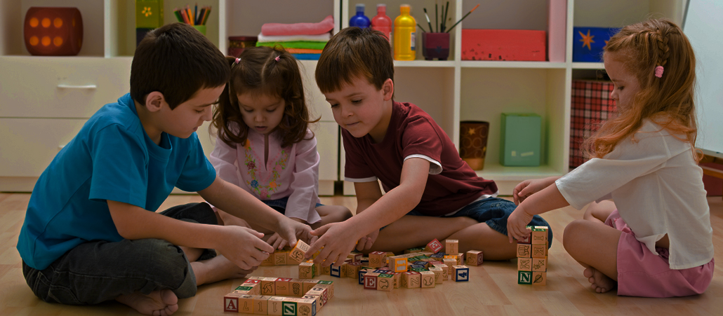 Kinder sitzen auf dem Boden und spielen mit Buchstabenklötzchen