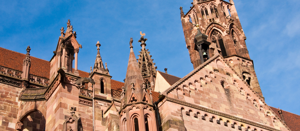 Vor blauem Himmel ist die seitliche Fassade einer rötlichen Sandsteinkirche zu sehen.