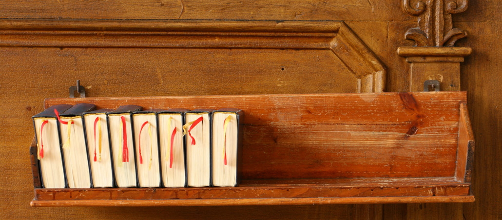 Mehrere Gesangbücher in einer Halterung an einer Kirchenbank.