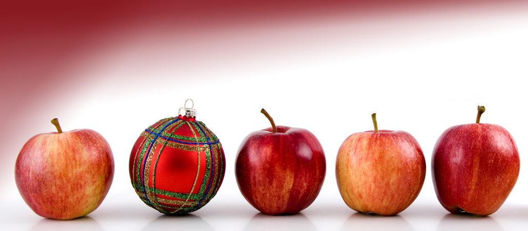 Äpfel in einer Reihe, dazwischen eine Christbaumkugel im Schottenkaro