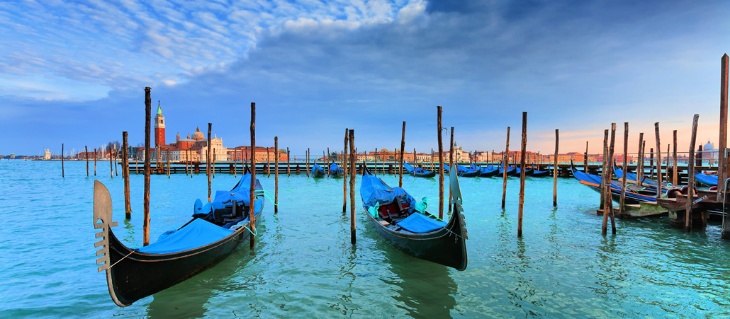 Blau-schwarze Gondeln gondeln im azzurblauen Wasser vor der Skyline Venedigs vor sich hin.