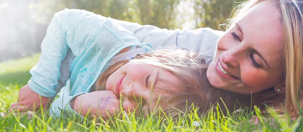 Eine Mutter liegt mit ihrer Tochter im Gras.