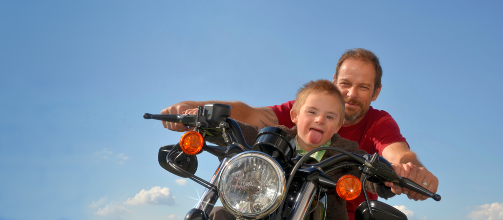 Vater und Sohn mit Downs-Syndrom auf einem Motorrad