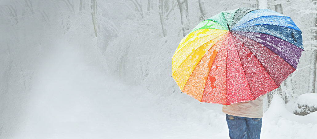 Mann mit großem Regenbogenschirm geht durch einen verschneiten Wald.