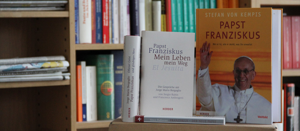 Vier Bücher über Papst Franziskus stehen vor einem vollen Bücherregal.