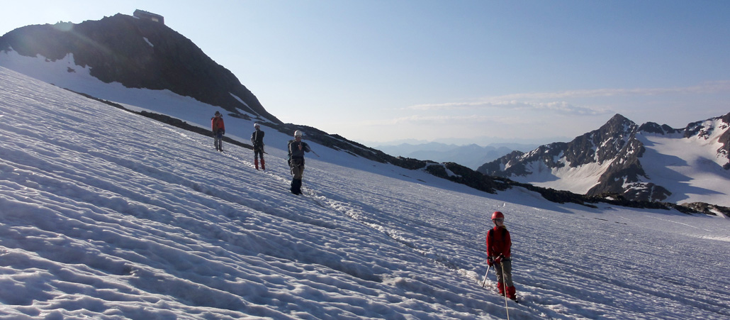 Ein Schneefeld, über das Bergsteiger mit Helm und Seil balancieren.