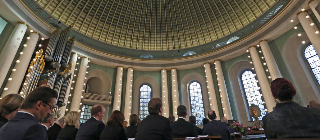 Die Kuppel der runden Hedwigskathedrale mit den Rücken von Abgeordneten im Vordergrund unten.