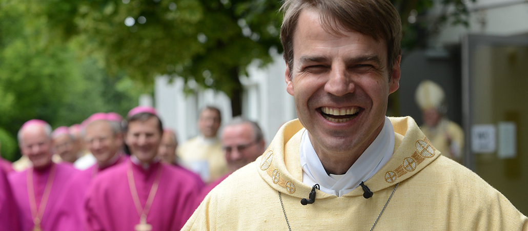 Pater Stefan Oster lacht vor dem Einzug in den Stephansdom im Hintergrund lachen Bischöfe.