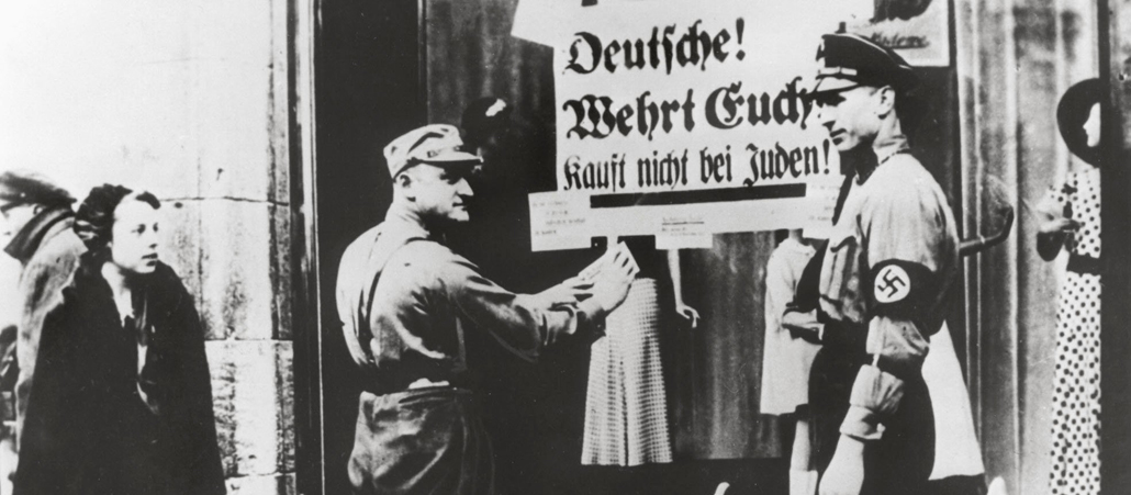 Zwei Nazis kleben Schilder an eine Schaufensterscheibe, um die anderen Deutschen zum Boykott ihrer Mitbrüger aufzurufen.