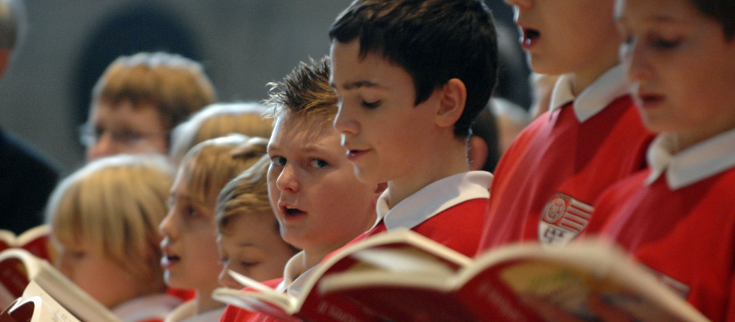 Mehrere Jungen schauen in ihre Musiknoten und singen im kirchlichen Jugendchor.