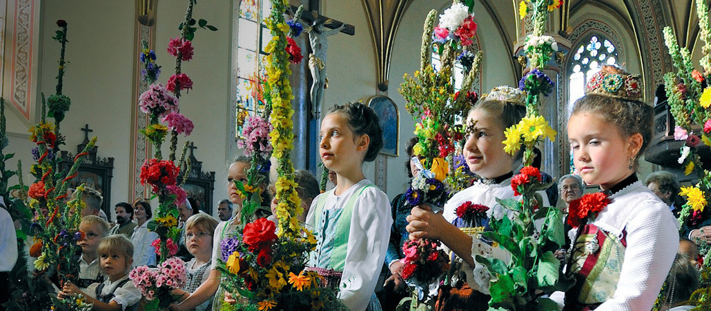 Ein Pfarrer segnet Kinder in Tracht mit Blumen an Mariä Himmelfahrt in der Kirche in Partenkirchen.