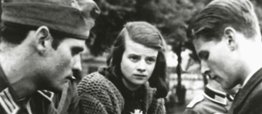 Hans Scholl in Uniform am linken Bildrand, Christoph Probst in zivil am rechten Bildrand. Dazwischen Sophie Scholl mit strengem Seitenscheitel, Strickjacke und ernstem Blick.