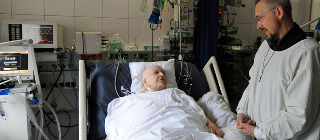 Pfarrer Walter Koll (Medizinische Universitäts-Poliklinik und Universitätsklinikum Bonn) spricht am Krankenbett mit einer Patientin.