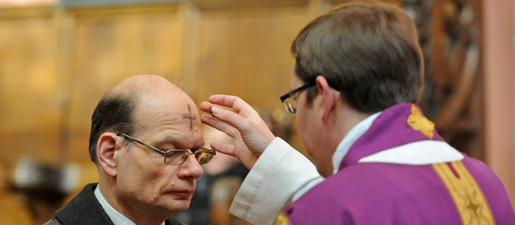 Ein Priester spendet einem Gottesdienstbesucher das Aschenkreuz.