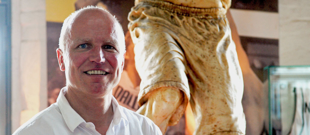 Thomas Nonte, seit März 2013 katholischer Sportpfarrer, steht vor einer antik anmutenden Sportlerstatue im Deutschen Sport __amp__ Olympia Museum in Köln.
