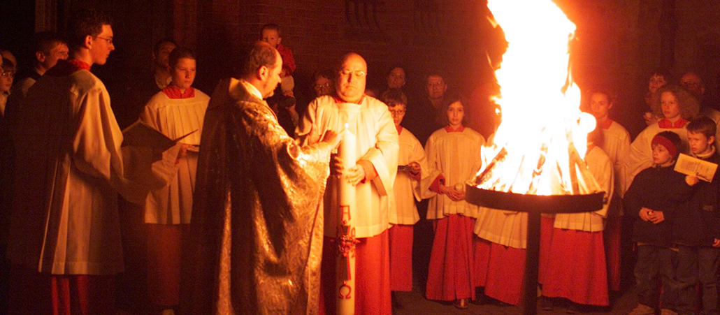 Ein Priester und die Gläubigen stehen um ein Osterfeuer.
