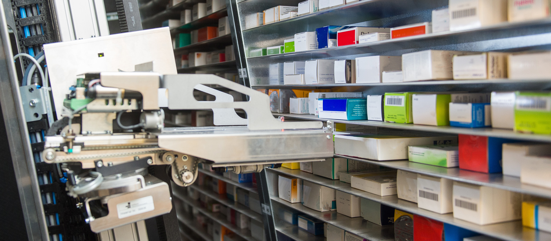 Der Arm eines Kommissionierautomaten sortiert Medikamente in ein Regal.