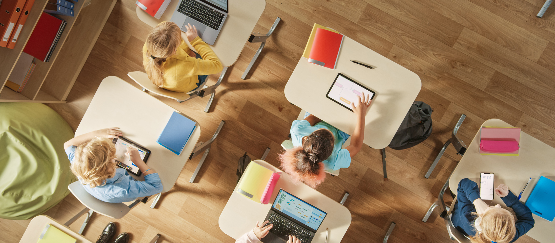 Schülerinnen und Schüler sitzen im Klassenraum und schauen auf Laptop, Tablet und Smartphone