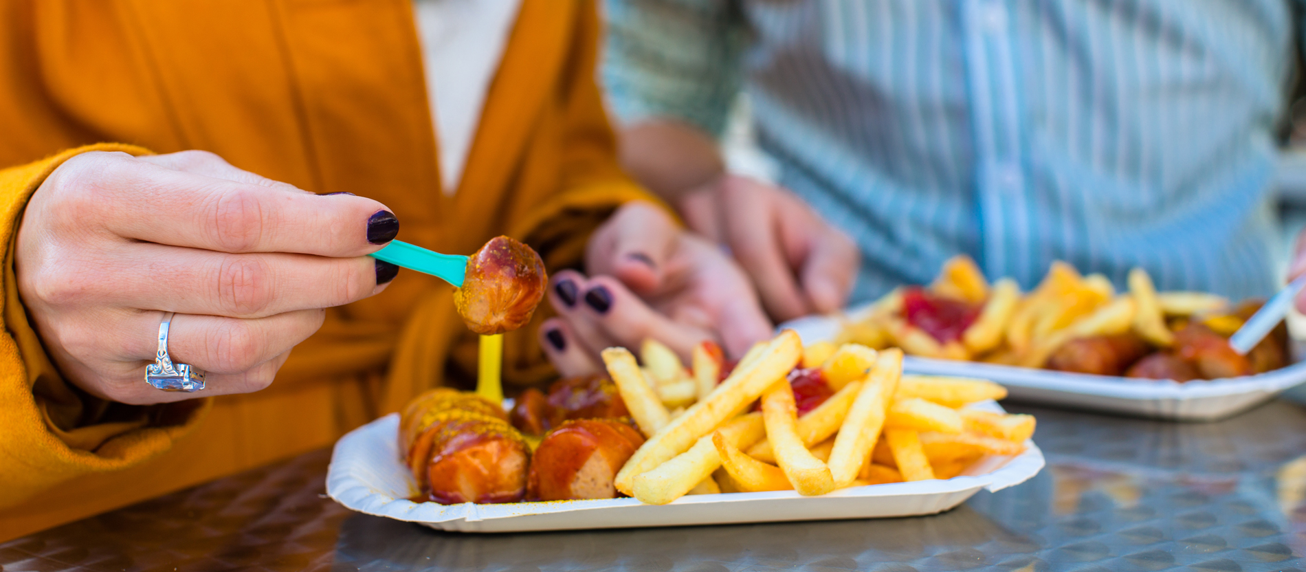Paar isst Currywurst und Pommes in einer Imbissbude