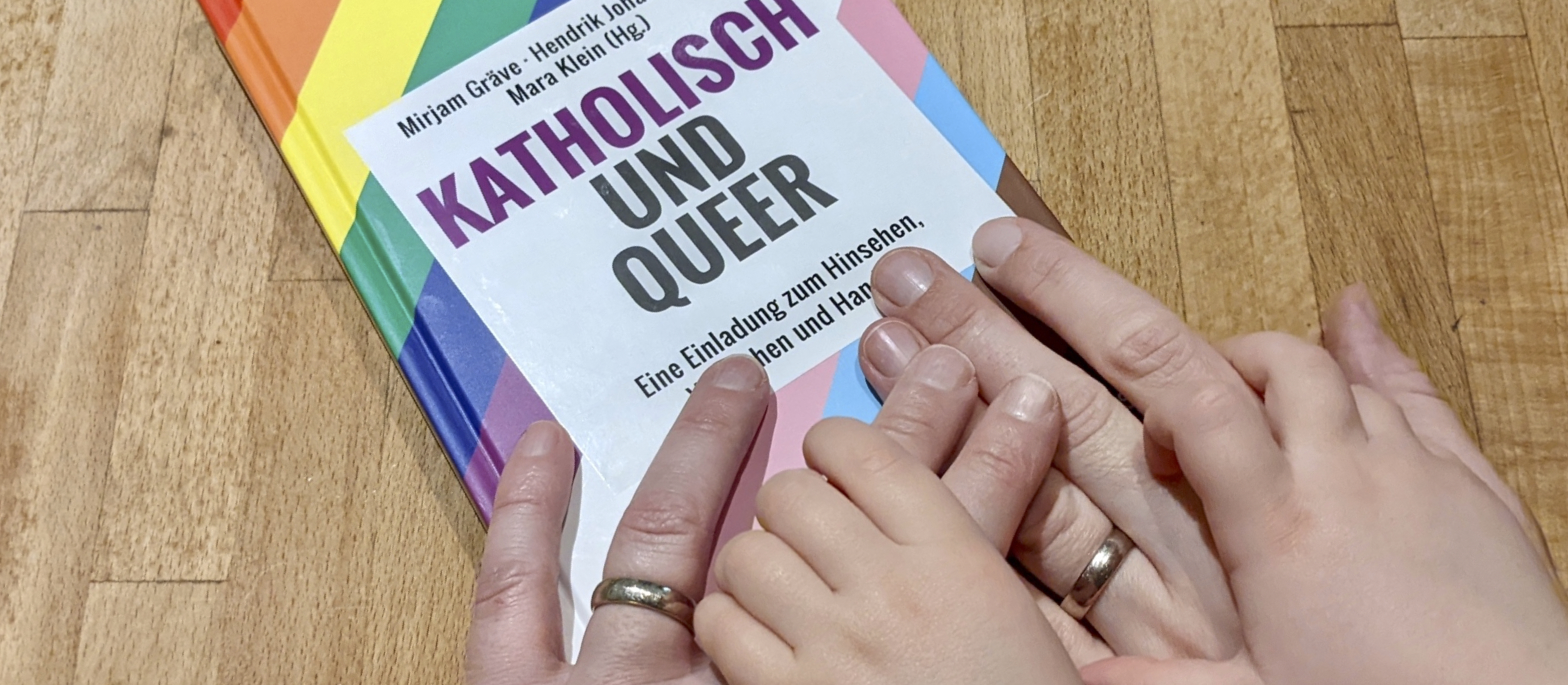 Hände liegen auf einem regenbogenfarbenen Buch