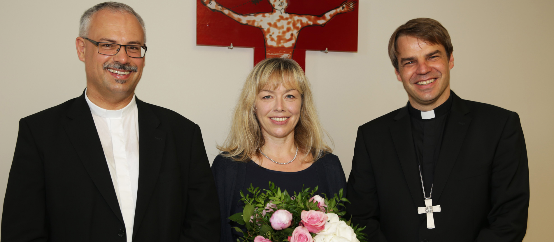 Der Generalvikar von Passau, Klaus Metzl, Antonia Murr, Kanzlerin der Diözese Passau und Bischof Stefan Oster stehen vor einem Kreuz.