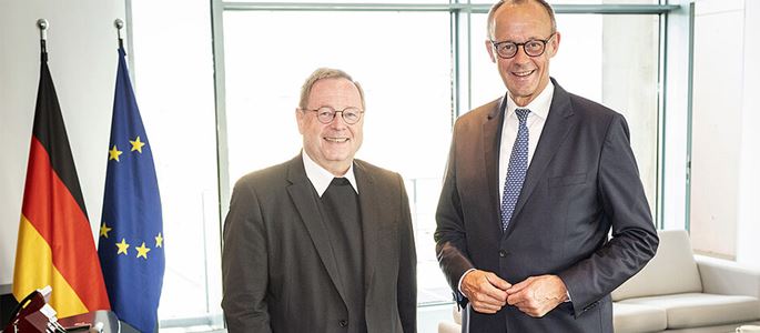 Bischof Georg Bätzing und Kanzler Friedrich Merz stehen neben den Flaggen der EU und Deutschlands