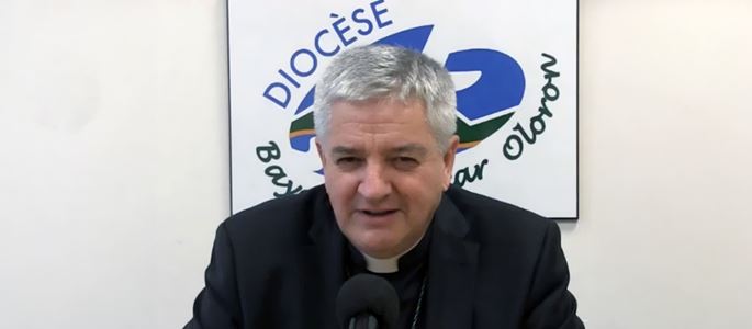 Bischof Marc Aillet bei einer Pressekonferenz vor dem Logo der Diözese Bayonne