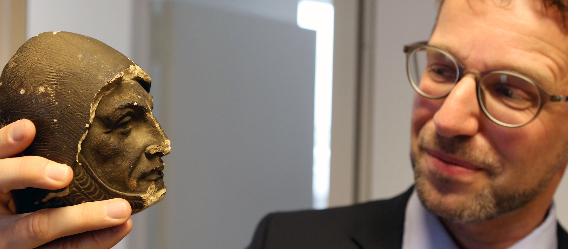 Ein Mann hält ein rußgeschwärztes Steinköpfchen in der Hand.
