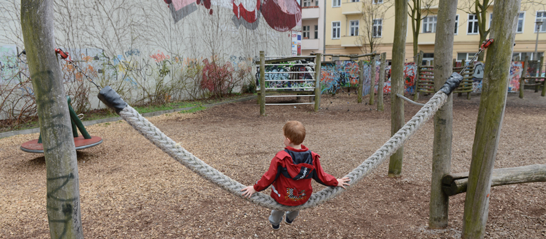 Ein Junge sitzt auf einer Schaukel auf einem Spielplatz in Berlin.