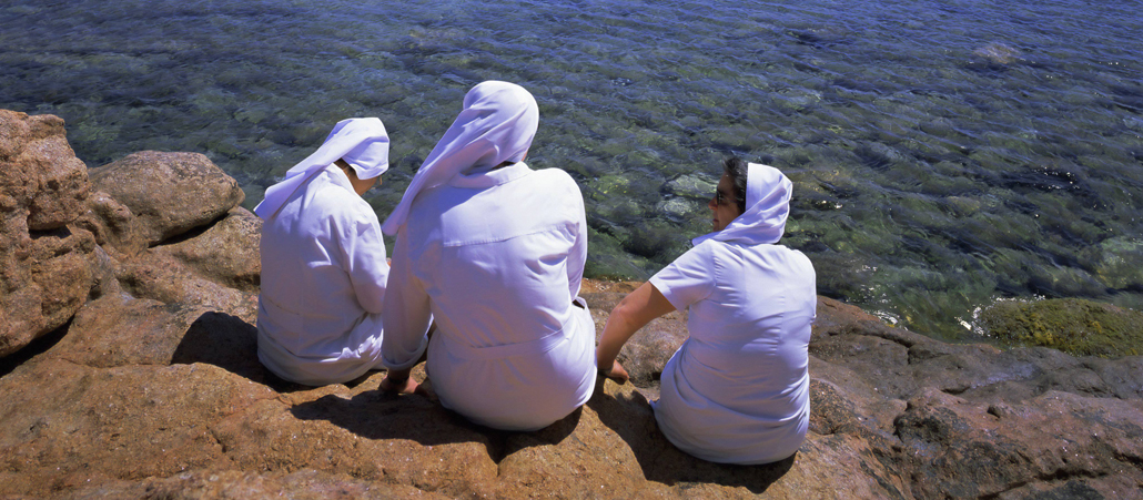 Drei spanische Nonnen sitzen auf einem Felsen am Meer.