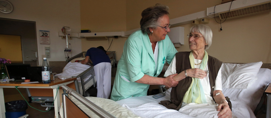 Eine grüne Dame hilft einer älteren Patientin in einem Hamburger Krankenhaus.