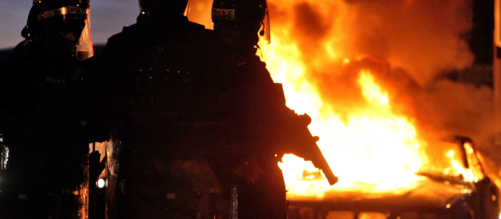 Union Flag protests. Riot police stand next to a burned out car after Loyalist protesters attacked police lines, in east Belfast. Picture date: Saturday January 12, 2013.