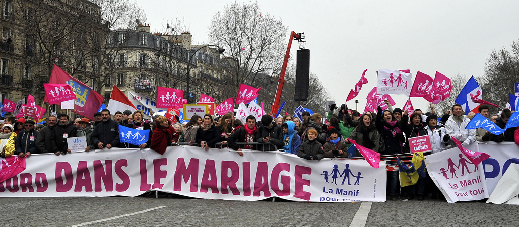 Eine Reihe aufgebrachter Demonstranten mit pinken Fahnen verschanzen sich hinter einem Spruchband.