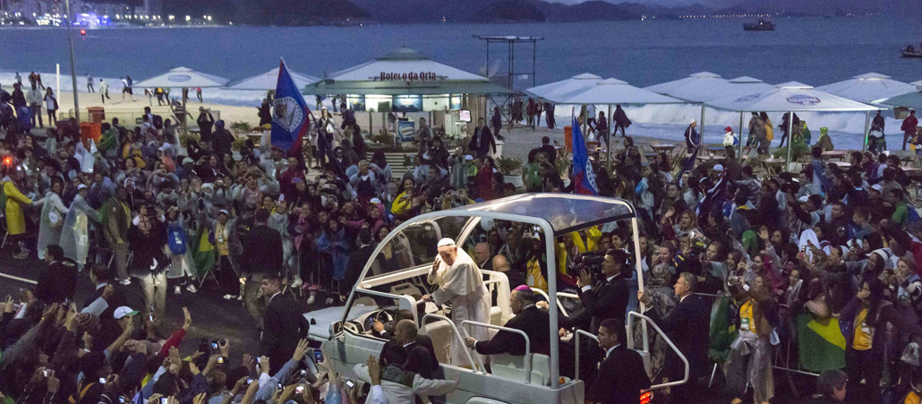 Vom Papamobil aus winkt Franziskus Jugendlichen zu. Im Hintergrund ist das Meer und die Copacabana zu sehen.