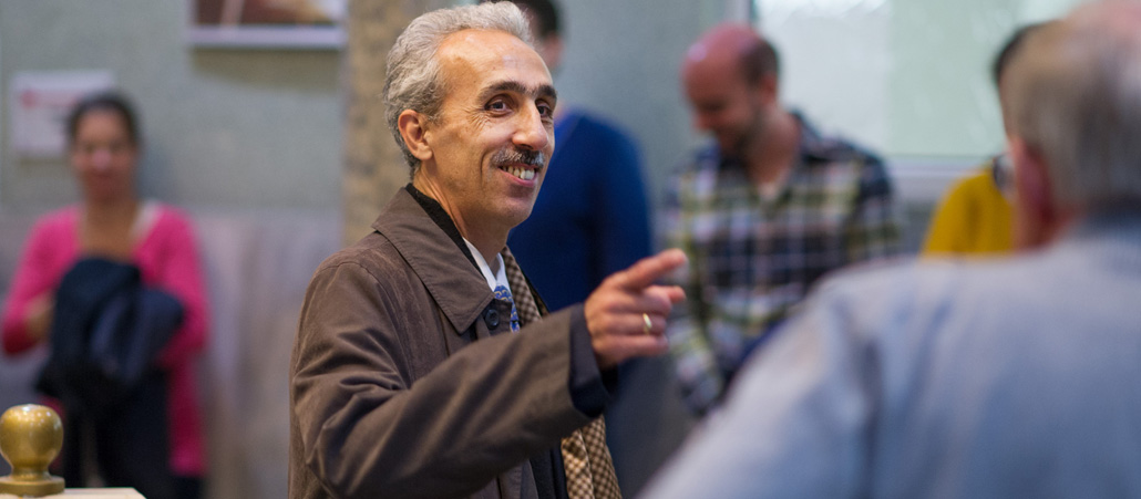 Mehrere Menschen sitzen in einem großen Raum auf dem Teppichboden.