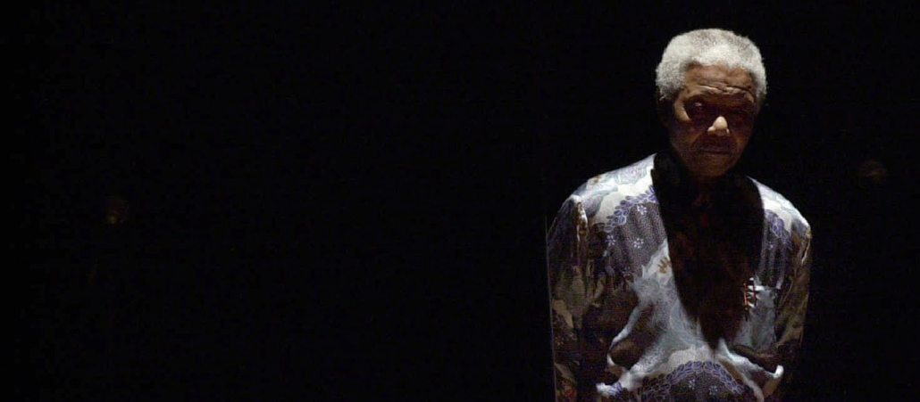 Nelson Mandela im Rampenlicht einer Bühne vor schwarzem Hintergrund.