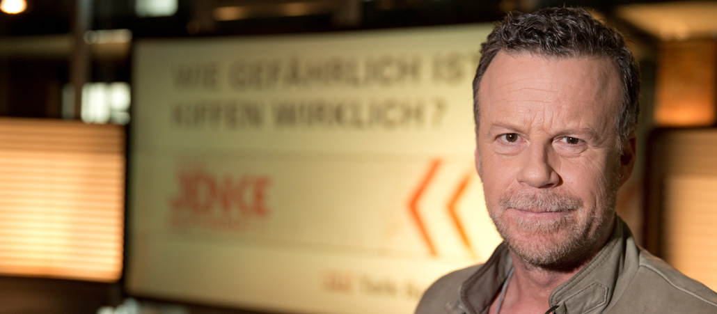 Jenke von Wilmsdorff vor einem Werbeplakta.