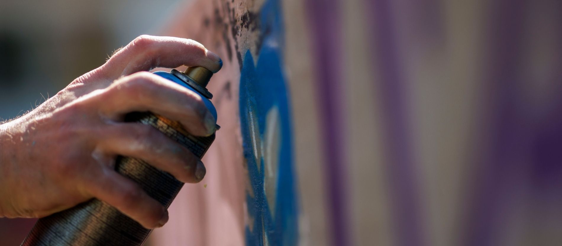 Ein Mann sprüht mit einer Spraydose ein Graffiti an eine Wand.