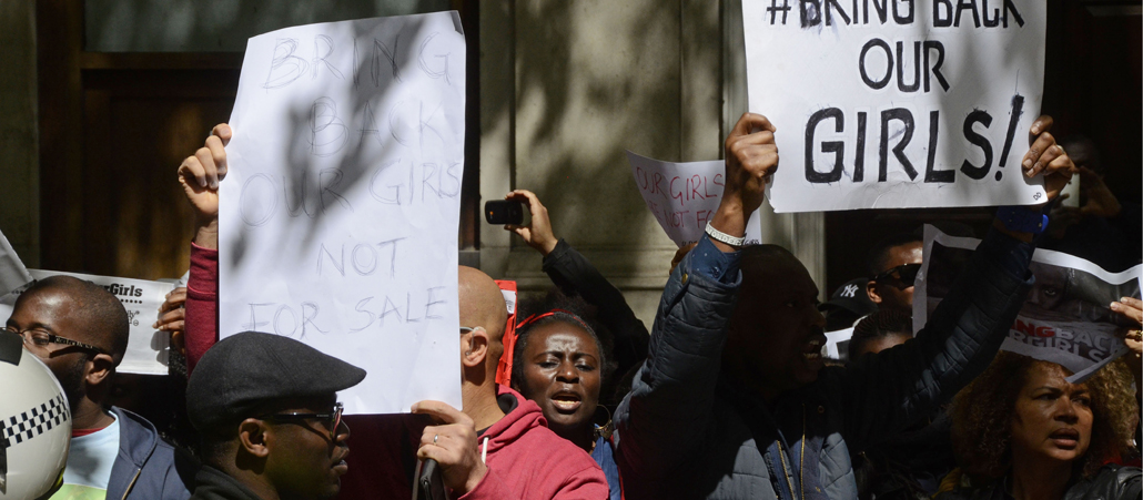 Mehrere farbige Menschen demonstrieren und halten ein Plakat mit dem Hashtag #BringBackOurGirls in die Höhe.