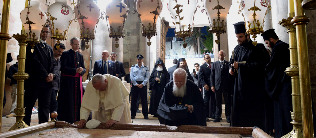 Der Papst (links) und der Patriarch (rechts) knien an der Grabplatte nieder; hinter ihnen stehen Sicherheitsleute und Popen.