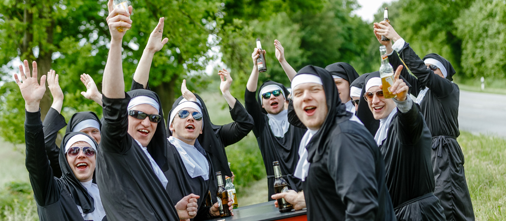 Junge Männer in Nonnenkostümen ziehen am Vatertag über die Landstraße und genehmigen sich einen Schluck aus der Flasche.