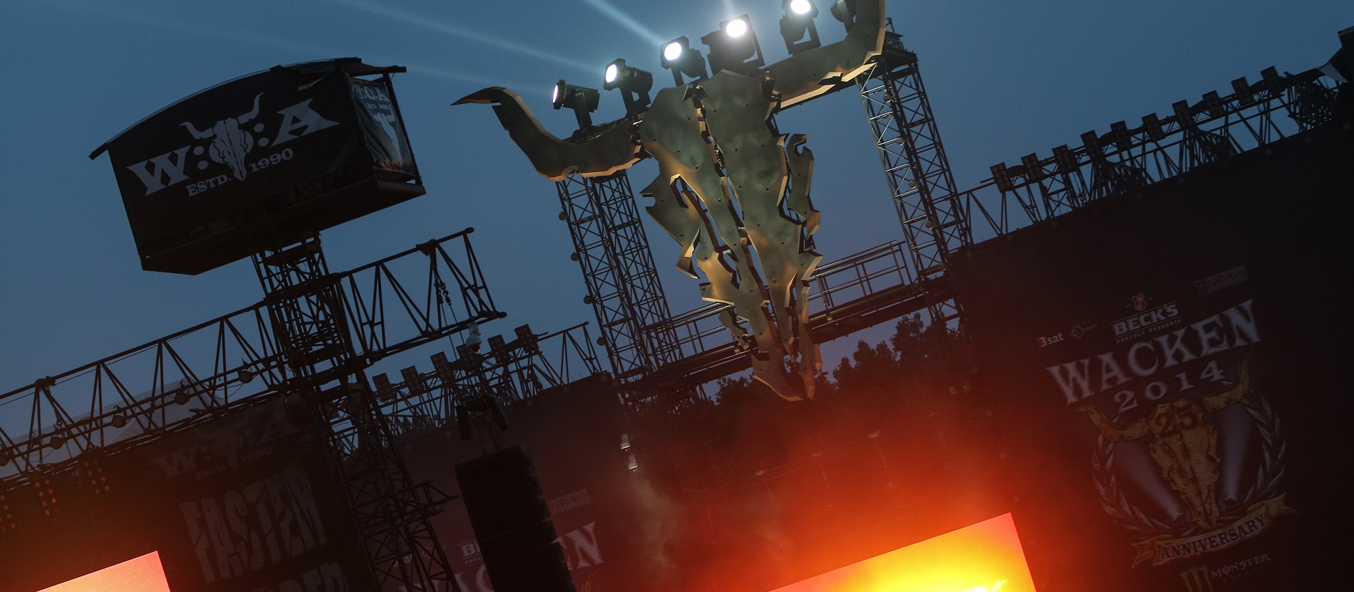 Scheinwerfer strahlen über dem Logo des Wacken-Festivals, einem riesigen Rinderschädel, der über der Hauptbühne aufgehängt ist.
