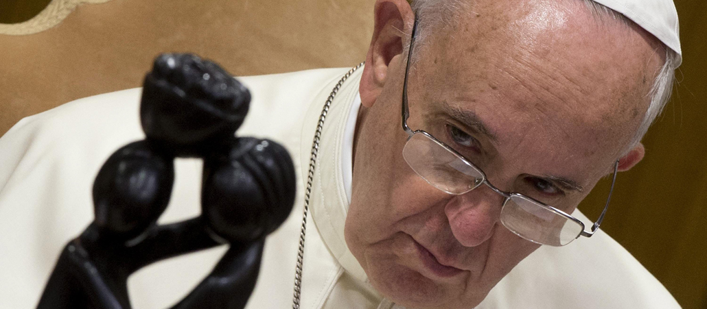 Papst Franziskus guckt auf eine kleine Statue.