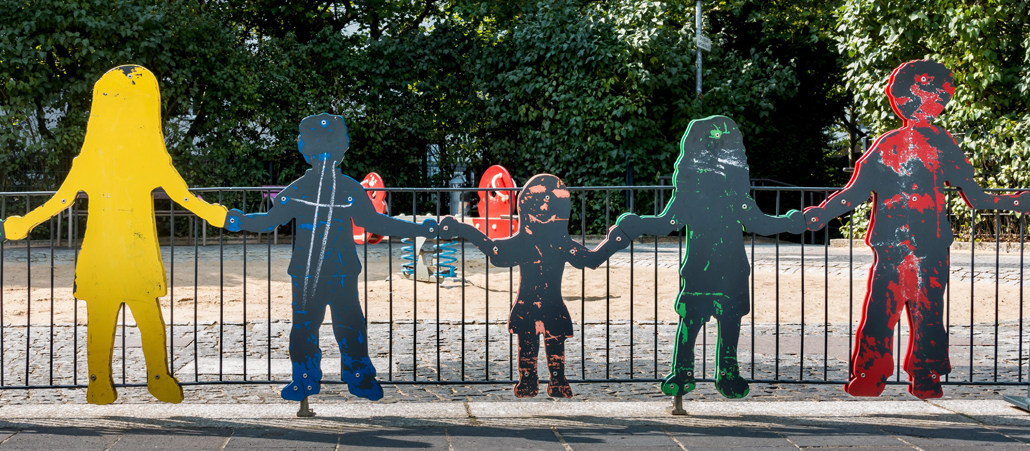 Holzfiguren in Lebensgröße stehen an einem Spielplatz.